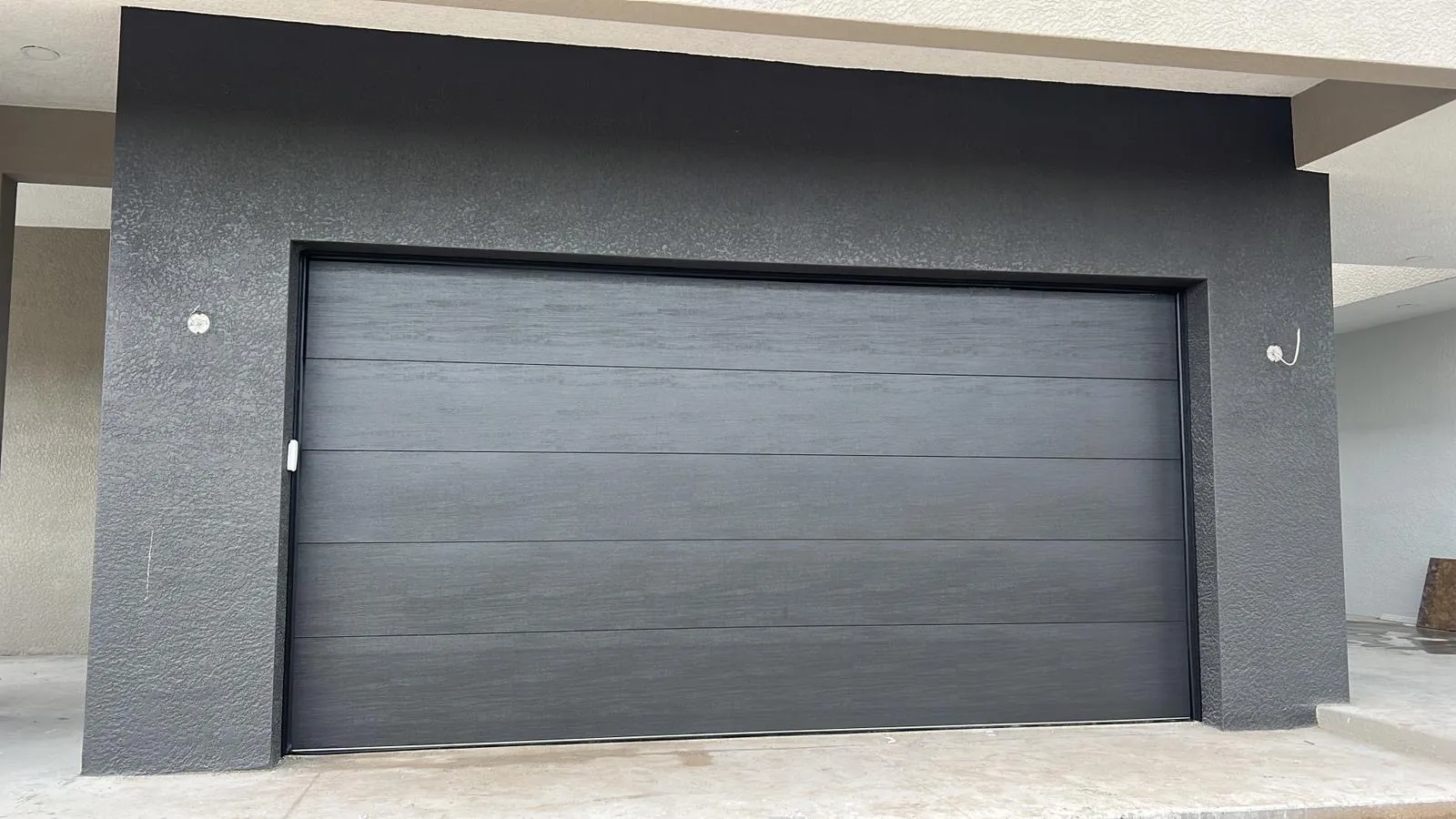 Modern black garage door with horizontal panels, set against a gray wall.