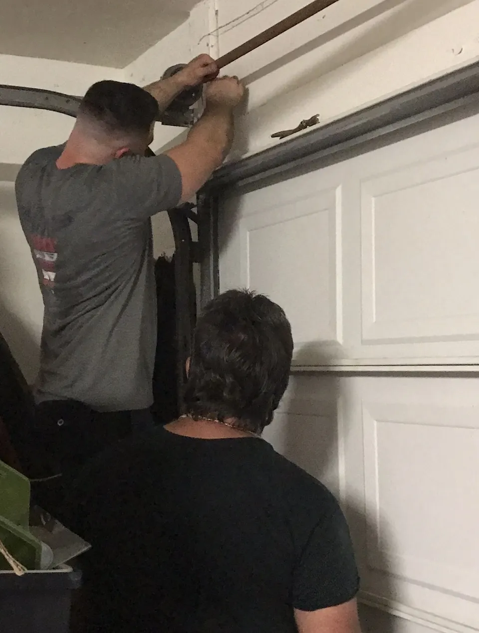 Contractor in work gear inspecting a garage door spring mechanism in a professional on-the-job setting